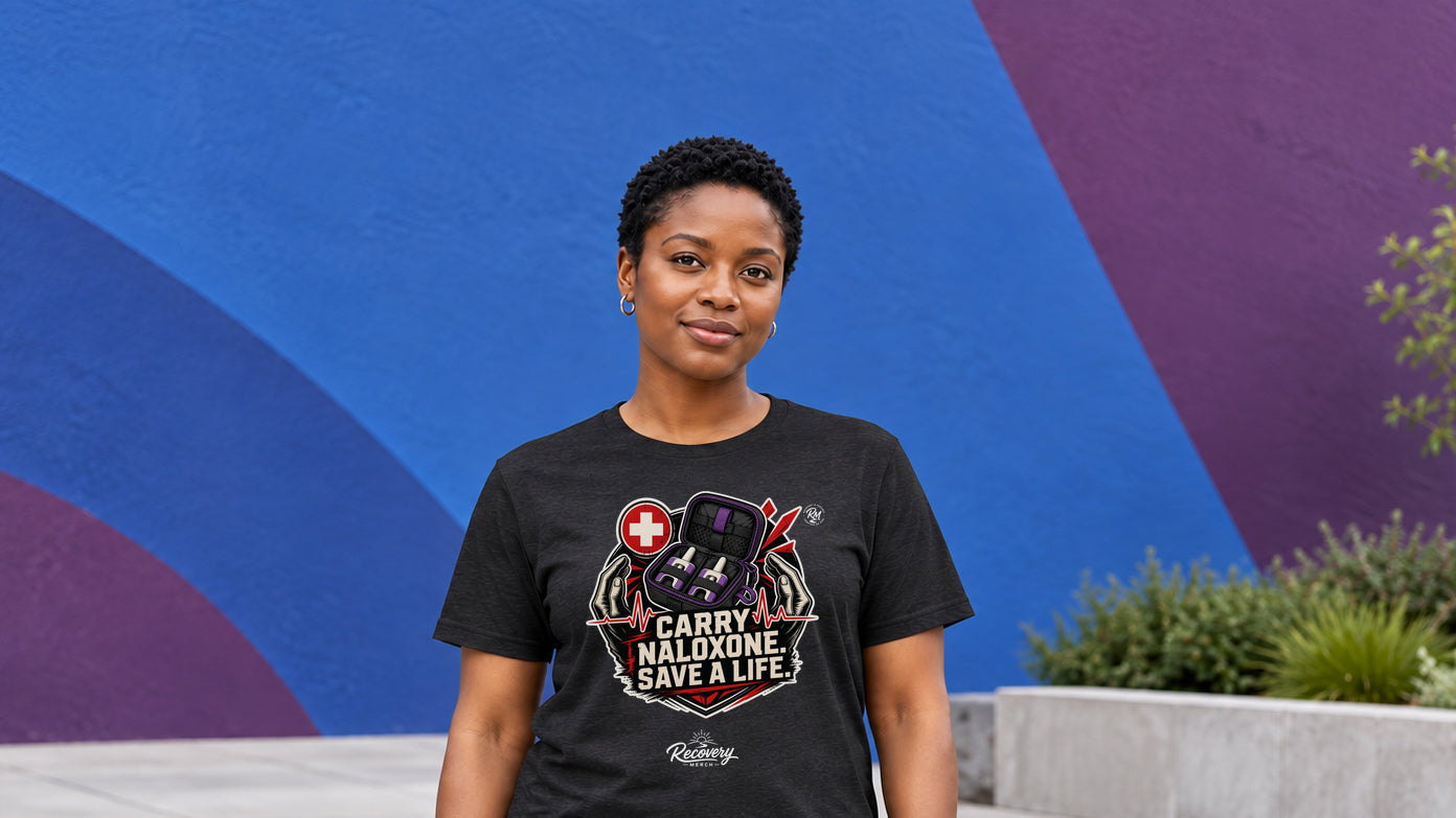Model wearing the Carry Naloxone Save A Life Recovery Merch T-shirt against a cobalt and plum wall
